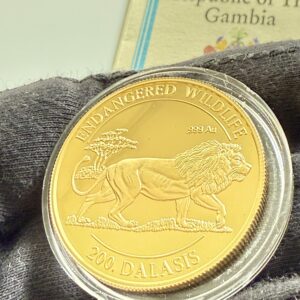 Gambia 1996 200 Dalasis Goldmünze Löwe Endangered Wildlife 1oz .999 Au Proof in transparenter Kapsel, COA der Republic of The Gambia im Hintergrund teilweise sichtbar.