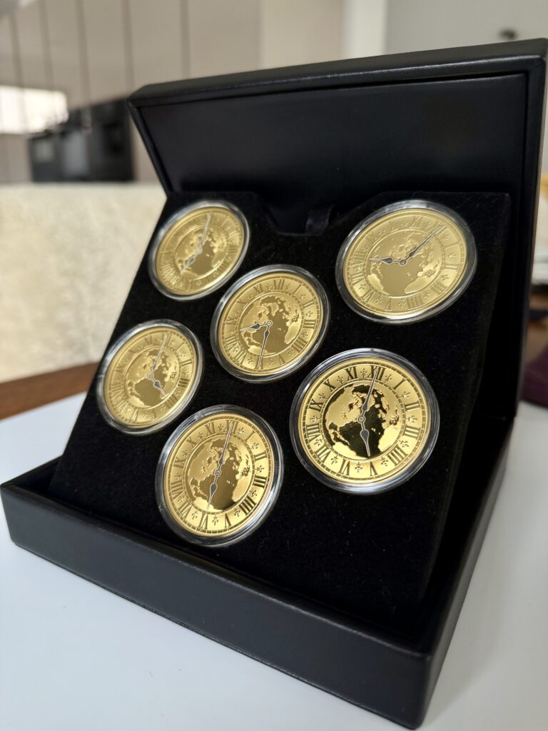 Kanada 2005 Zeitzonen Kanadas Gold Proof Set – sechs 300-Dollar-Goldmünzen im geöffneten schwarzen Präsentationsetui, jede Münze gekapselt mit römischem Zifferblatt, Weltkarten-Motiv und unterschiedlichen Uhrzeiten auf schwarzer Velourseinlage.
