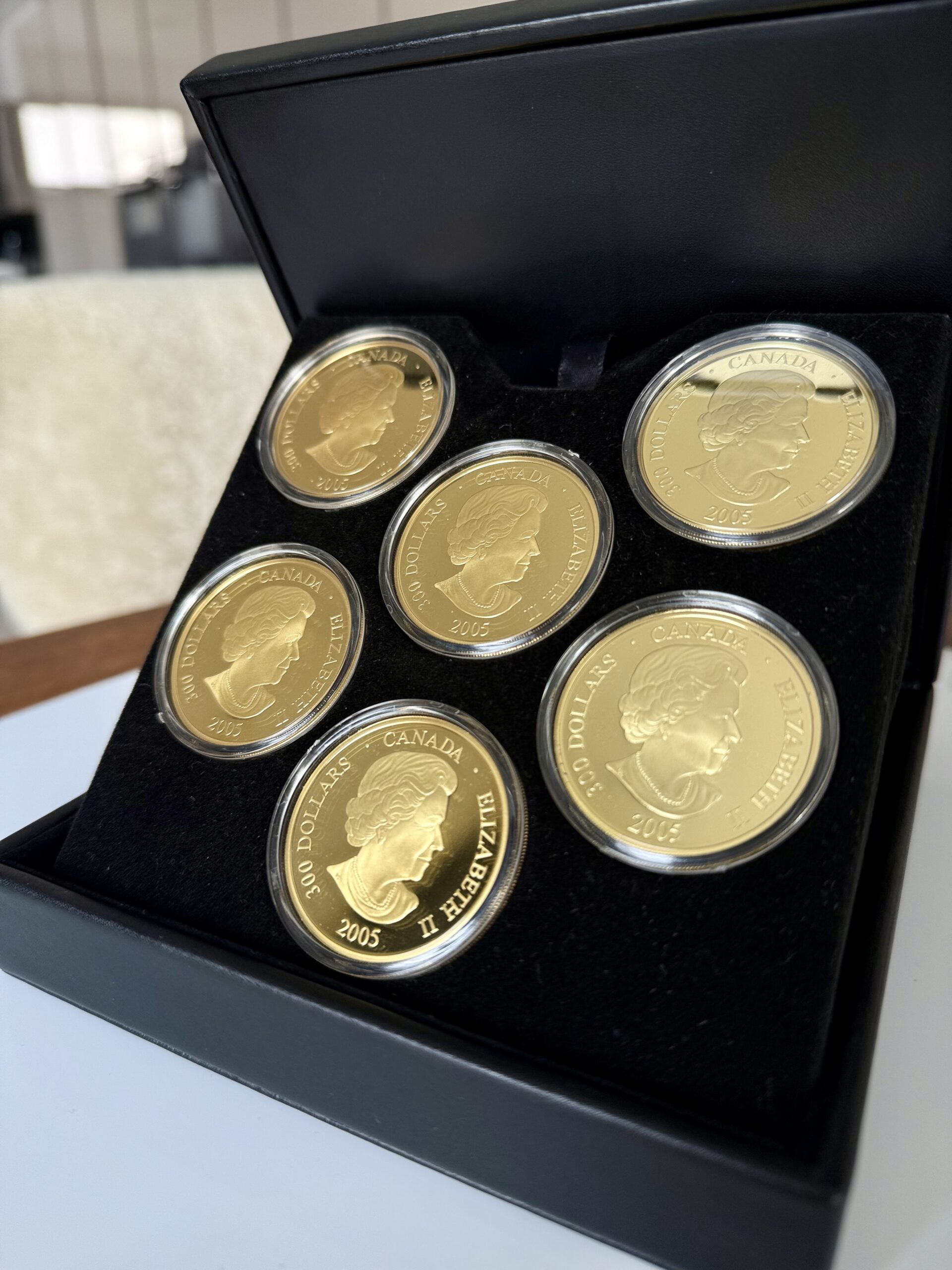 kanada-2005-300-dollar-zeitzonen-kanadas-5oz_2 Kanada 2005 Zeitzonen Kanadas Gold Proof Set – sechs 300-Dollar-Goldmünzen im geöffneten schwarzen Präsentationsetui, jede Münze gekapselt mit römischem Zifferblatt, Weltkarten-Motiv und unterschiedlichen Uhrzeiten auf schwarzer Velourseinlage.