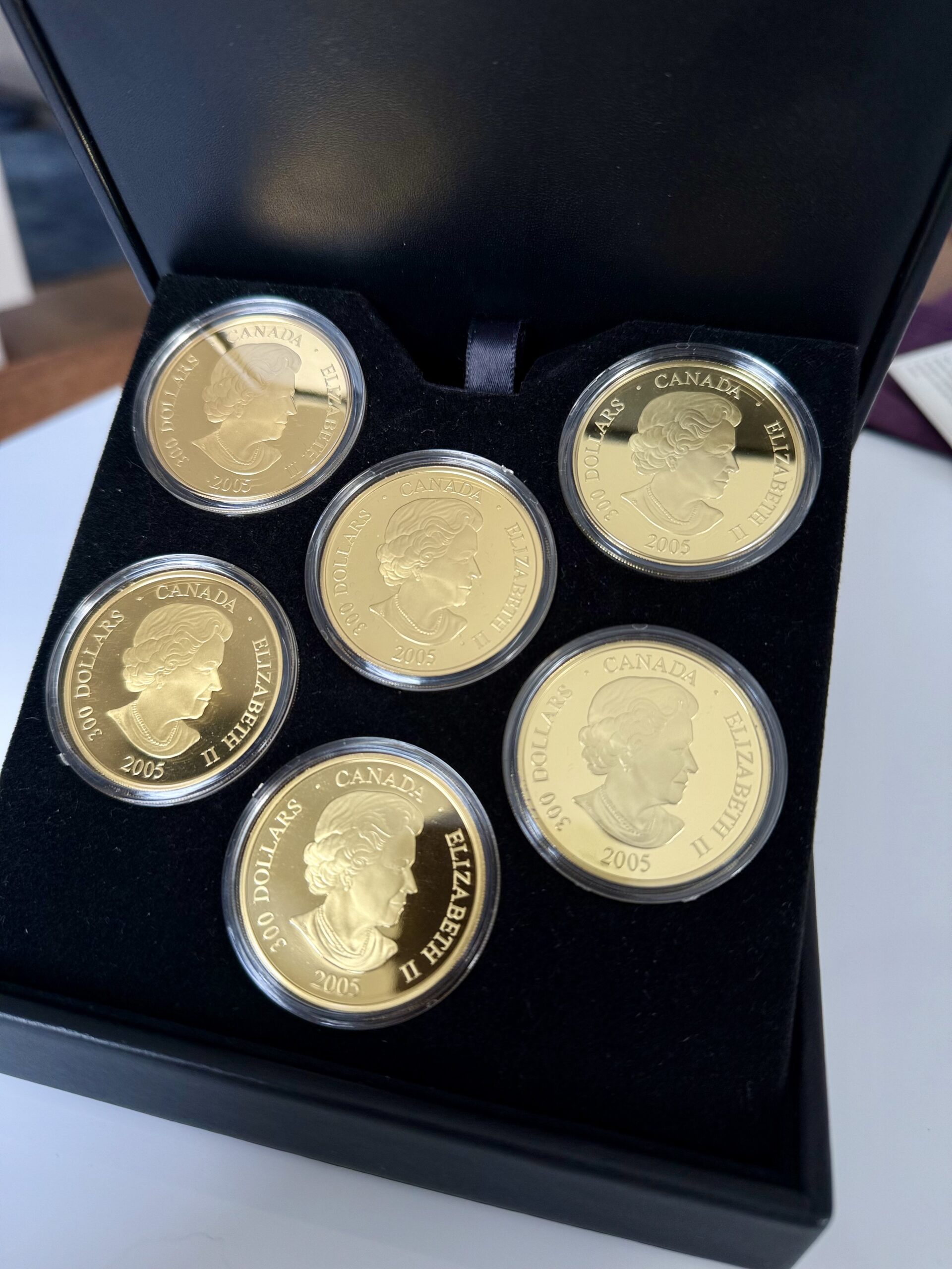 kanada-2005-300-dollar-zeitzonen-kanadas-5oz_5 Kanada 2005 Zeitzonen Kanadas Gold Proof Set – sechs 300-Dollar-Goldmünzen im geöffneten schwarzen Präsentationsetui, jede Münze gekapselt mit römischem Zifferblatt, Weltkarten-Motiv und unterschiedlichen Uhrzeiten auf schwarzer Velourseinlage.