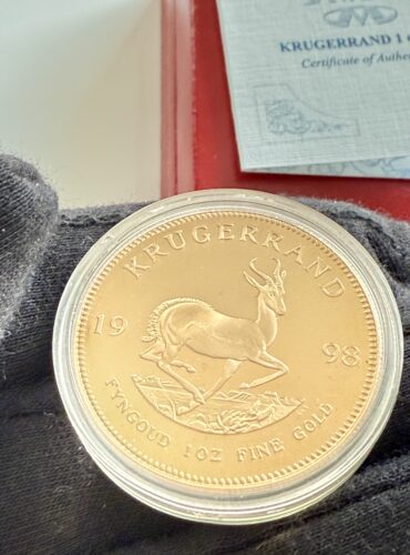 Krugerrand 1998 1oz Gold, Springbock-Seite, gekapselt vor roter Box, COA der South African Mint teilweise sichtbar.