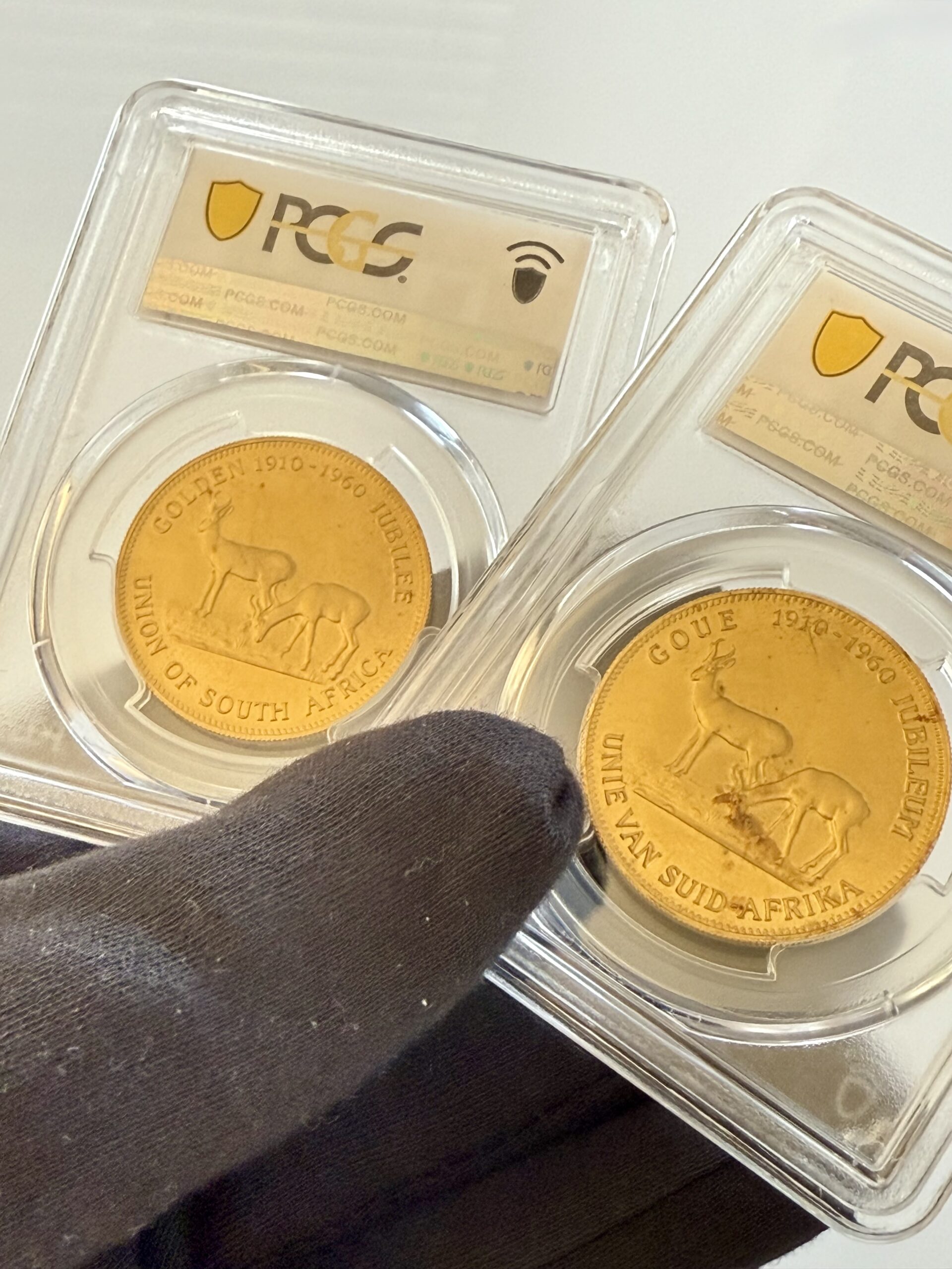 suedafrika-1960-chamber-of-mines-1oz-gold-afrikaans-und-englisch.pcgs_2 Zwei PCGS-Slabs nebeneinander mit Südafrika 1960 Chamber of Mines 1oz Gold. Links Afrikaans-Variante Hern-U37a PCGS MS67, rechts English-Variante Hern-U37b PCGS MS68, jeweils mit Turmmotiv.