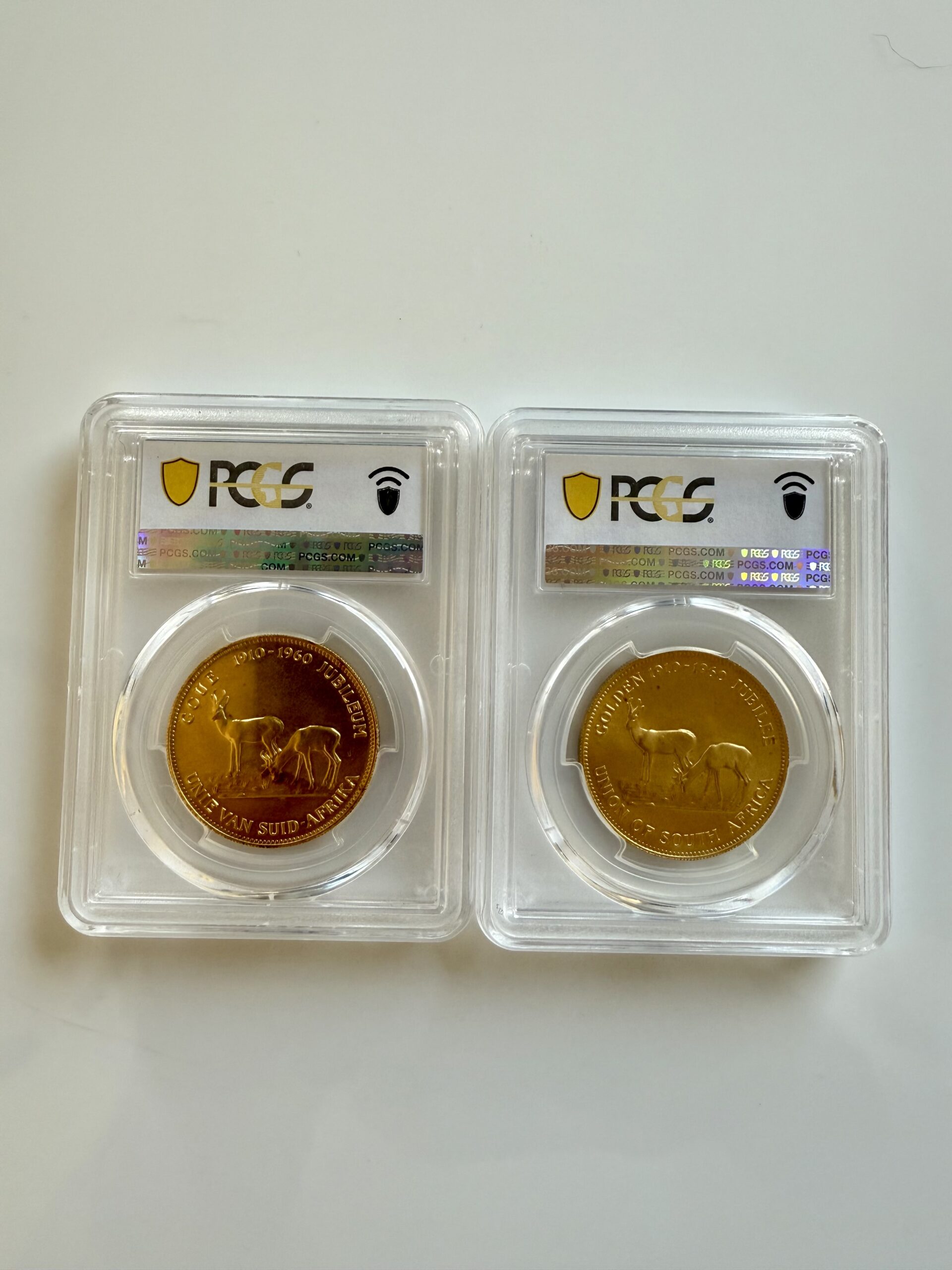 suedafrika-1960-chamber-of-mines-1oz-gold-afrikaans-und-englisch.pcgs_3 Zwei PCGS-Slabs nebeneinander mit Südafrika 1960 Chamber of Mines 1oz Gold. Links Afrikaans-Variante Hern-U37a PCGS MS67, rechts English-Variante Hern-U37b PCGS MS68, jeweils mit Turmmotiv.