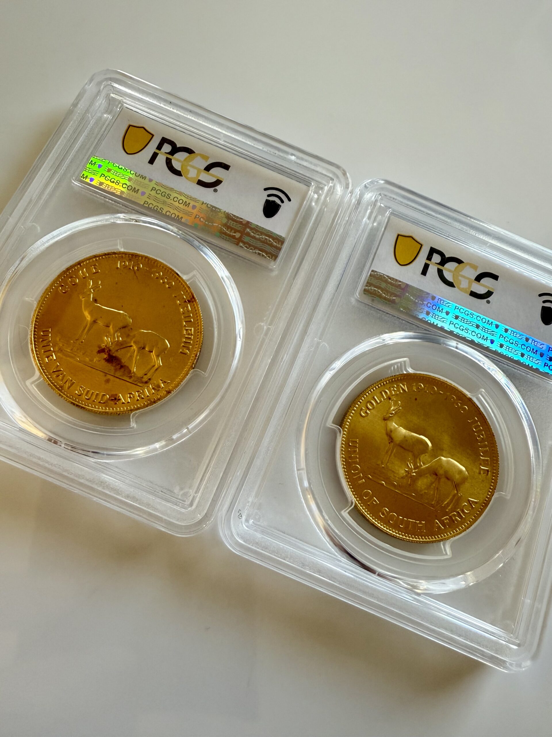 suedafrika-1960-chamber-of-mines-1oz-gold-afrikaans-und-englisch.pcgs_5 Zwei PCGS-Slabs nebeneinander mit Südafrika 1960 Chamber of Mines 1oz Gold. Links Afrikaans-Variante Hern-U37a PCGS MS67, rechts English-Variante Hern-U37b PCGS MS68, jeweils mit Turmmotiv.
