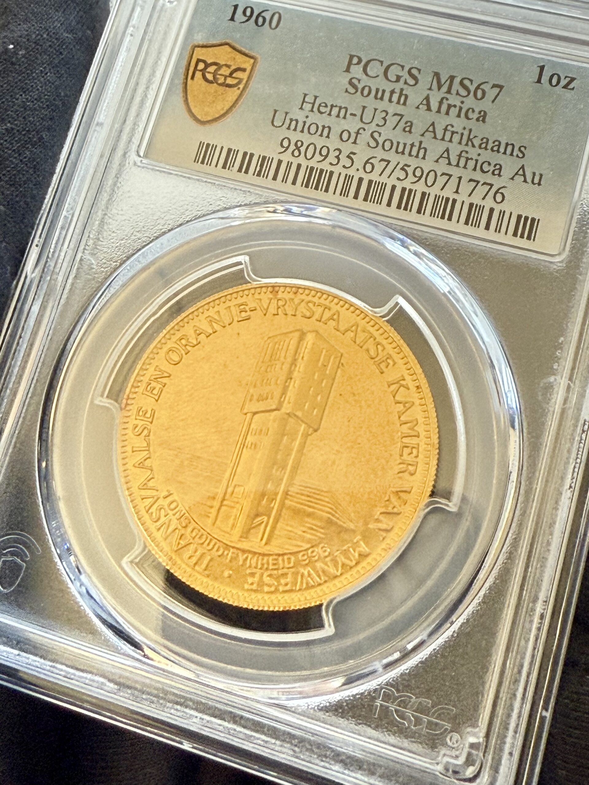 suedafrika-1960-chamber-of-mines-1oz-gold-afrikaans-und-englisch.pcgs_8 Südafrika 1960 Chamber of Mines 1oz Gold, Afrikaans-Version im PCGS-Holder MS67; Turm-Motiv mit umlaufender afrikaanssprachiger Legende, Label mit „Hern-U37a Afrikaans“.