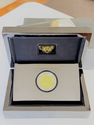 Moneta d'oro American Liberty del 2019 in una confezione di presentazione aperta con custodia nera, capsula inserita e certificato di autenticità parzialmente visibile sullo sfondo.