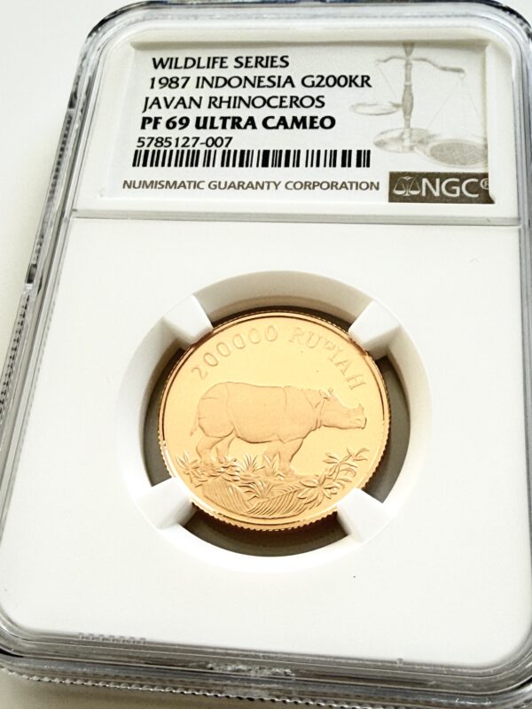 NGC-zertifizierte Goldmünze aus Indonesien von 1987 mit dem Motiv eines Javanischen Nashorns. Auf dem Label steht „Wildlife Series - 1987 Indonesia G200KR - Javan Rhinoceros - PF 69 Ultra Cameo“ mit der Zertifizierungsnummer 5785127-007. Die Münze ist in einem NGC-Slab auf weißem Hintergrund fotografiert.