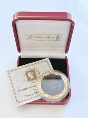 Original presentation case of an Isle of Man gold coin with the red presentation box open, containing the coin in a capsule and an accompanying certificate. The coin is inscribed "Penny Black - 150th Anniversary - Crown", the certificate "Certificate of Proof Penny Black", and the lid reads "Pobjoy Mint - England UK".