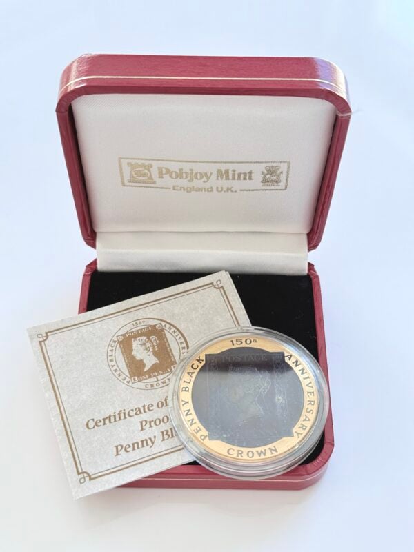 Original presentation case of an Isle of Man gold coin with the red presentation box open, containing the coin in a capsule and an accompanying certificate. The coin is inscribed "Penny Black - 150th Anniversary - Crown", the certificate "Certificate of Proof Penny Black", and the lid reads "Pobjoy Mint - England UK". 