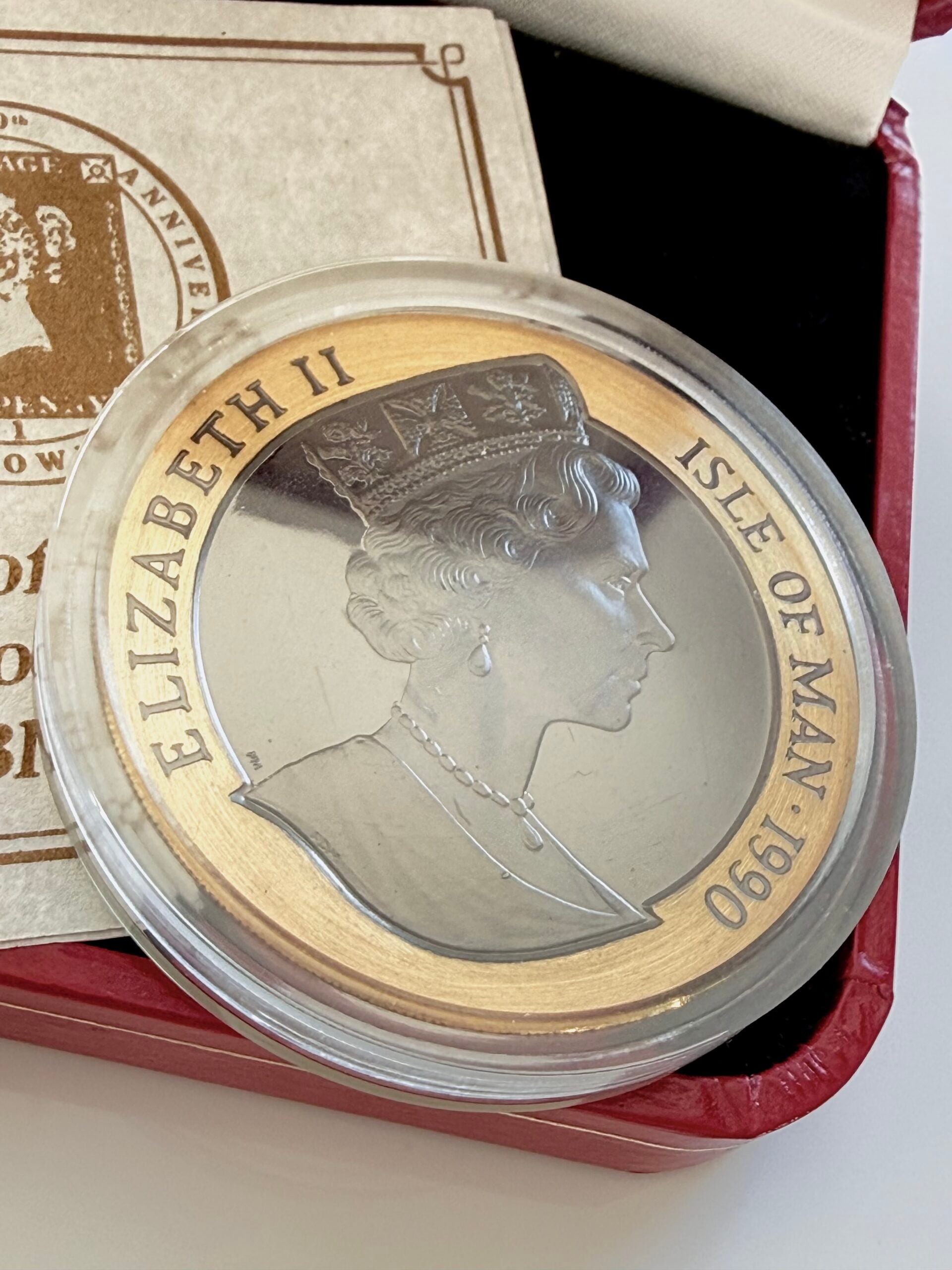 Estuche original de una moneda de oro de la Isla de Man con caja de presentación roja abierta, moneda en cápsula y certificado adjunto. La moneda lleva la inscripción “Penny Black - 150th Anniversary - Crown”, el certificado “Certificate of Proof Penny Black” y la tapa dice “Pobjoy Mint - England UK”.
