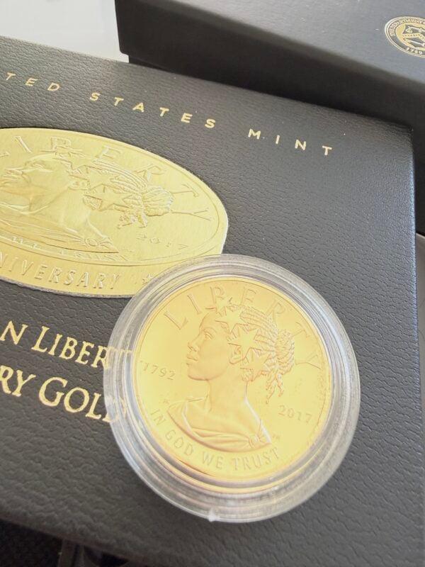 A 2017 US gold coin, American Liberty, in its capsule, photographed on its original black presentation box. Visible is the modern portrait of Liberty with a crown of stars, the year 2017, and the inscription "In God We Trust."
