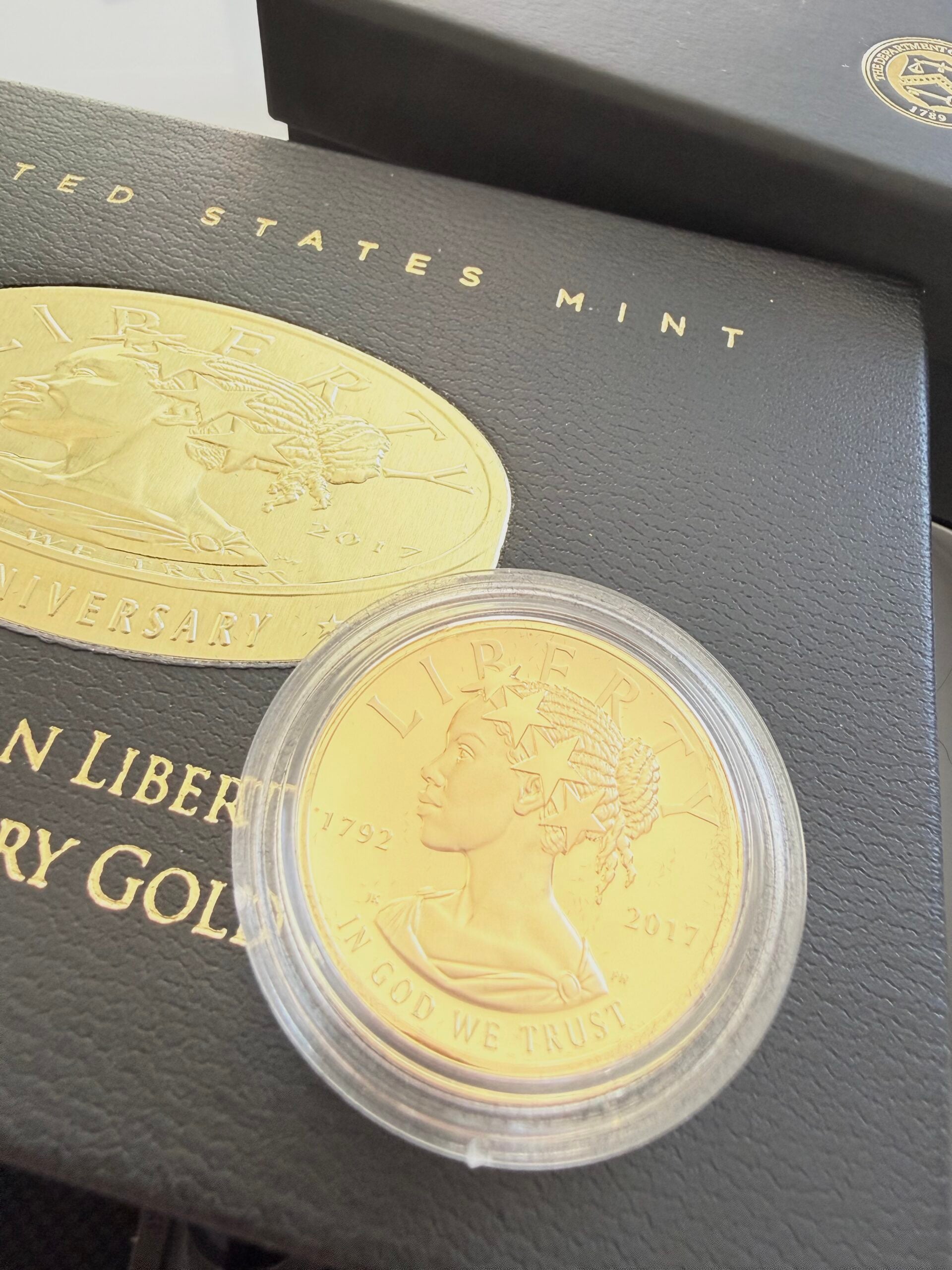 2017 US gold coin American Liberty in capsule, photographed on the original black presentation box. The image shows the modern portrait of Liberty with a star crown, the year 2017 and the inscription "In God We Trust".